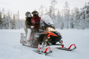 Akaslompolo Finland Winter Engagement with couple riding snowmobile