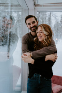 Akaslompolo Finland Winter engagement at glass cabin couple laughing and embracing