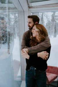 Akaslompolo Finland Winter Engagement couple looking out window of Arctic Lodge glass cabin