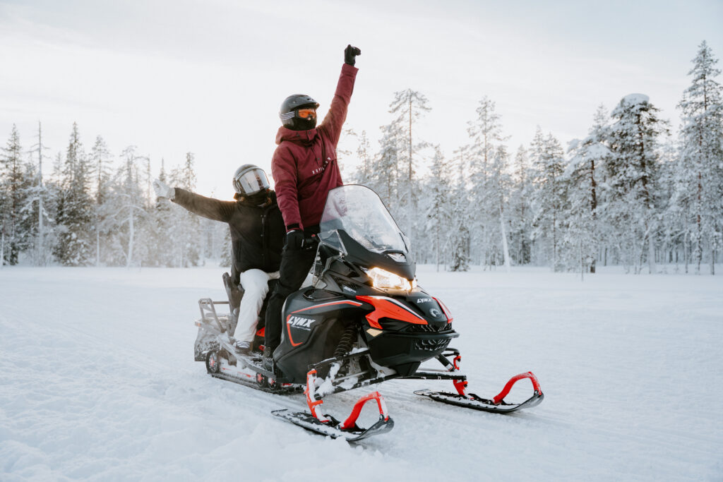 Engaged couple snowmobiling together in the snowy forests of Äkäslompolo, Finland during winter