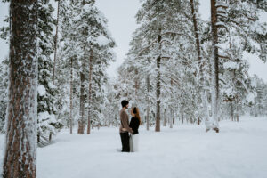 Engaged couple snowshoeing together in the snowy forests of Äkäslompolo, Finland during winter