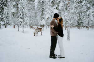 Akaslompolo Finland Winter Engagement couple kissing in the snow with earmuffs and reindeer