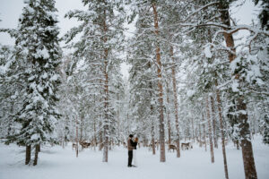 Akaslompolo Finland Winter Engagement wide shot of tall trees, couple, and reindeer