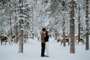 Akaslompolo Finland Winter Engagement couple kissing in the snow with reindeer all around and trees