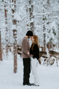 Engaged couple spending time with reindeer during a winter engagement session in Äkäslompolo, Finland