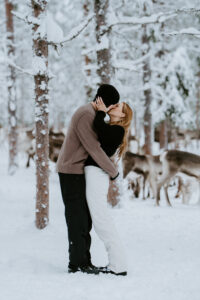 Akaslompolo Finland Winter Engagement couple kissing with reindeer around them