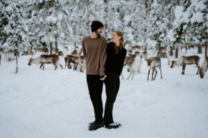 Akaslompolo Finland Winter Engagement couple back to back trying to kiss with reindeer