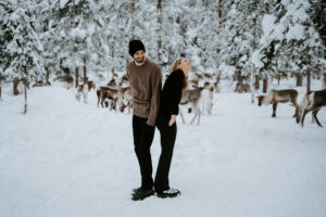 Akaslompolo Finland Winter Engagement couple back to back laughing with reindeer and trees
