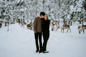 Akaslompolo Finland Winter Engagement couple kissing with many reindeer and snow in the trees