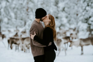 Akaslompolo Finland Winter Engagement couple kissing with reindeer in the background