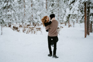 Engaged couple spending time with reindeer during a winter engagement session in Äkäslompolo, Finland