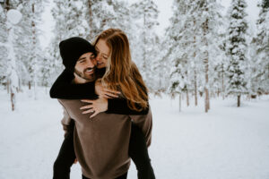 Akaslompolo Finland Winter Engagement couple doing piggy back ride in the snow