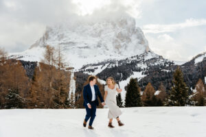 Passo Gardena Dolomites Winter Engagement, woman and man frolicking in the snow with Sassolungo in the background