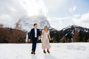 Passo Gardena Dolomites Winter Engagement, girl and guy walk hand in hand towards camera