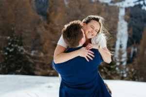 Passo Gardena Dolomites Winter Engagement, guy kisses girl as she jumps on him in the snow