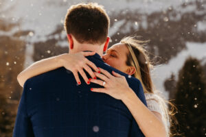 Passo Gardena Dolomites Winter Engagement, close up of ring on hand while woman kisses man and the snow falls