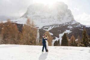 Passo Gardena Dolomites Winter Engagement, couple embracing as strong wind blows snow