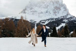 Passo Gardena Dolomites Winter Engagement, woman and man smiling and running towards camera