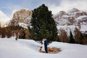 Passo Gardena Dolomites Winter Engagement, man and woman kiss in front of tree