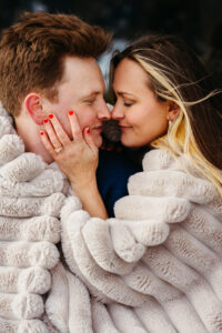 Passo Gardena Dolomites Winter Engagement, man and woman wrapped in cozy blanket to keep warm from the snow