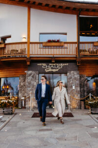 Passo Gardena Dolomites Winter Engagement, couple looks super cool with sunglasses walking out of fancy hotel