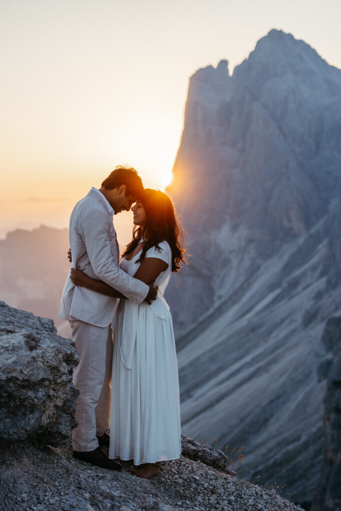 Couple at sunrise on top of Seceda with the sun poking from behind the mountain