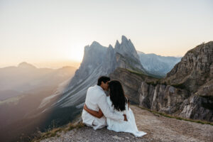 Engaged couple at Seceda during sunrise, sitting and kissing