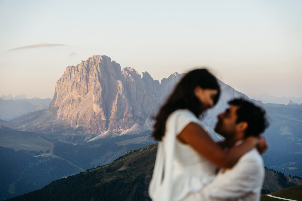 Proposal photo shoot in the Dolomites at sunrise on top of Seceda, with couple out of focus and langkofel in focus