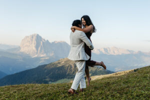 Man picks up his fiance during their engagement session at Seceda with Langkofel and Platkofel in the background