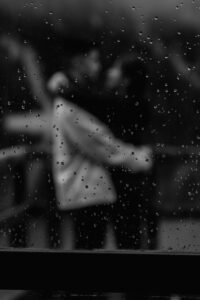 Creative black and white photo with sharpness on water droplets on the window with couple in the back ground of Lago di Braies engagement