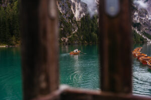 Looking through the fence at couple boating across Lago di Braies during their engagement