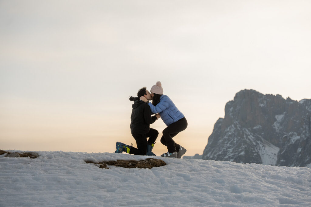 Bride to be kissing groom to be just after proposal during sunrise light on Alpe di Siusi in winter