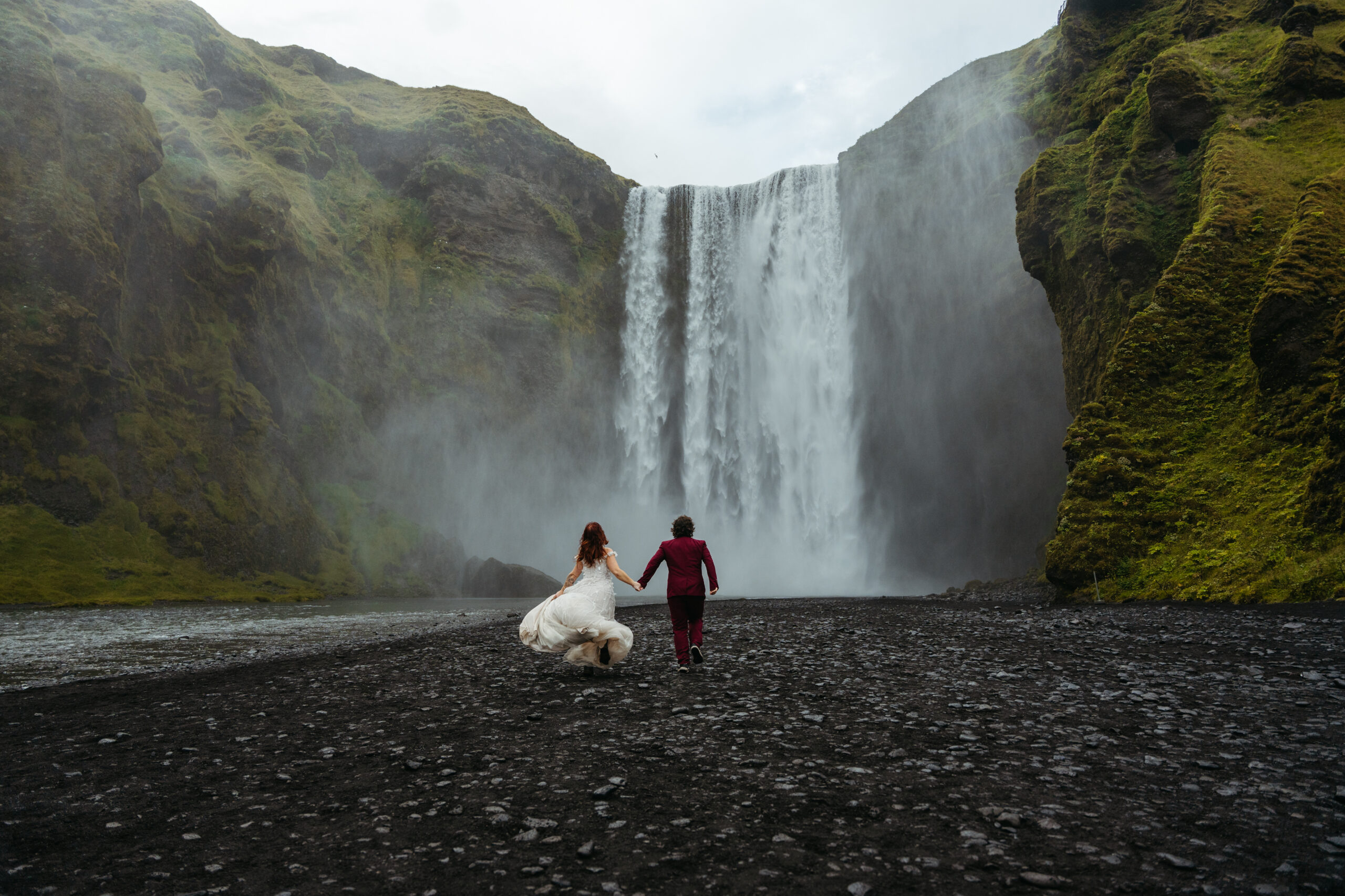 Couple in Iceland running towards waterfall during elopement
