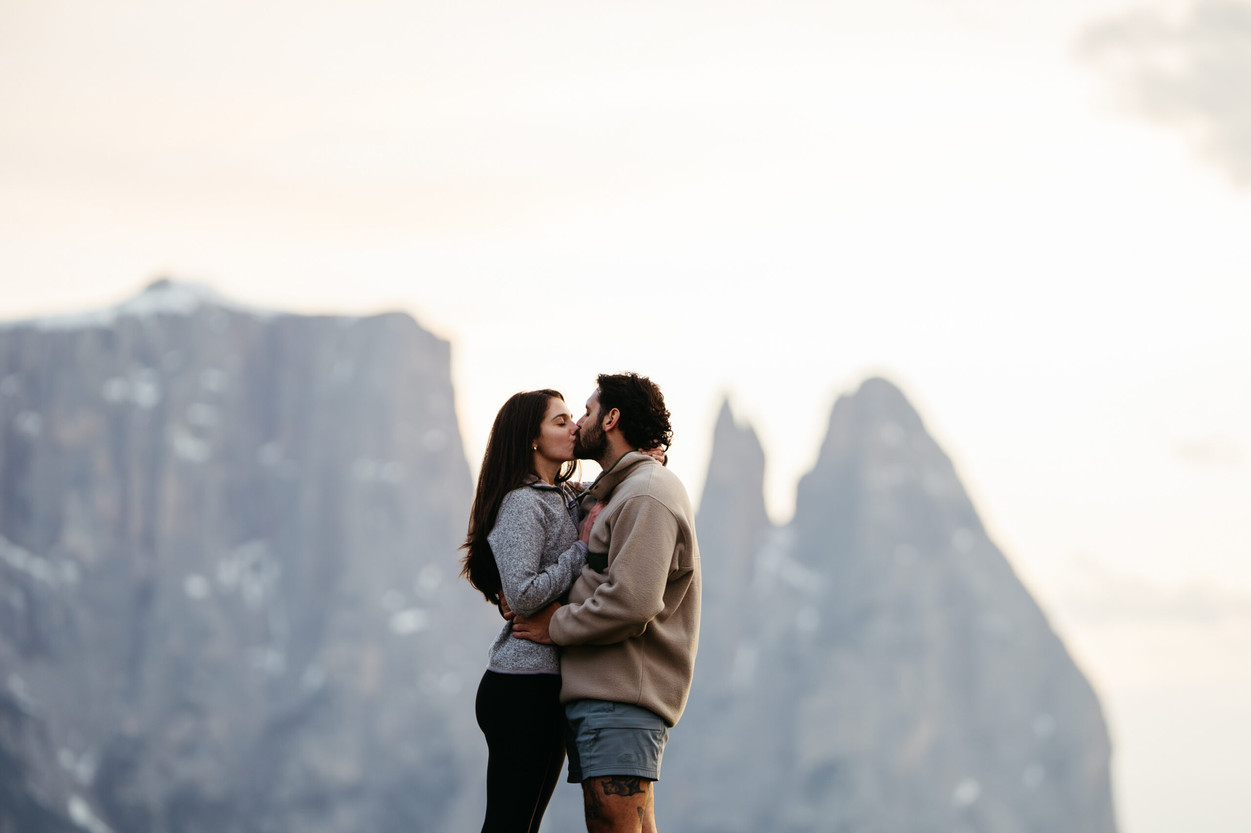 Engaged couple kissing on Alpe di Siusi with Schlern, Santner peak, and Euringer peak in the background
