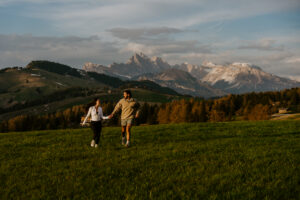 Sunset at Seiser Alm with newly engaged couple running towards the camera and Seceda in the background