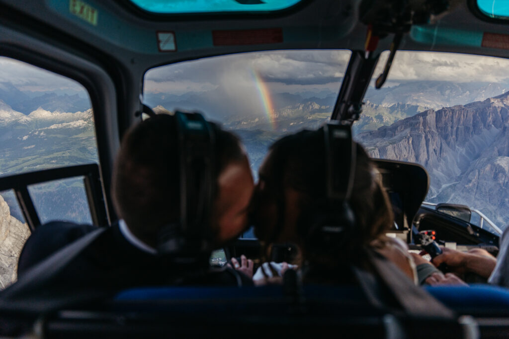 Bride and groom kissing during their helicopter elopement with a rainbow in the background