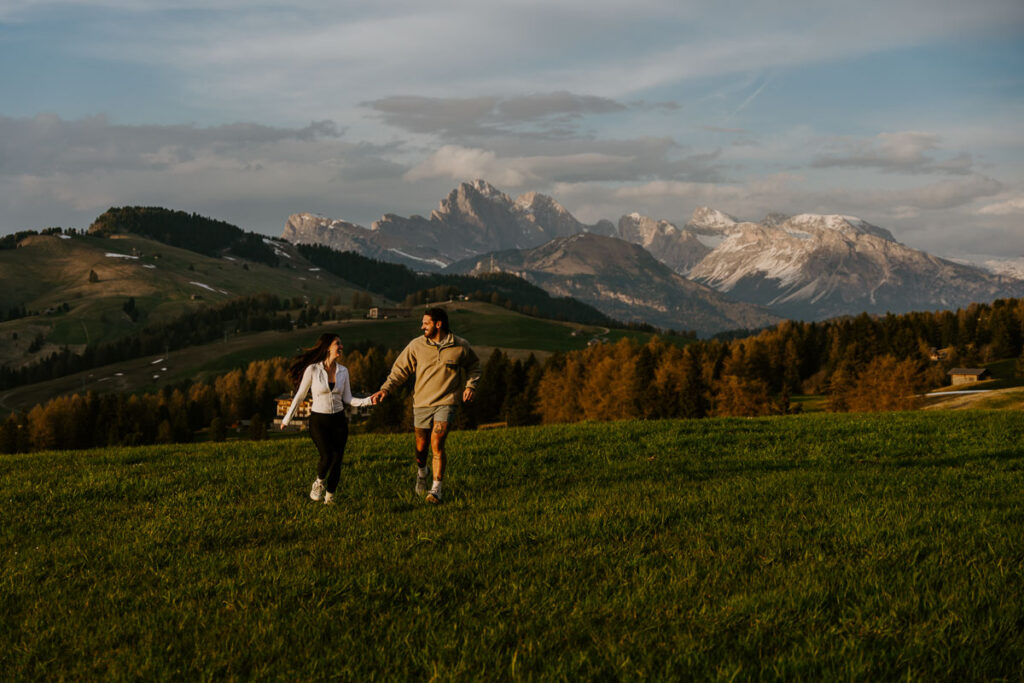 Adventurous couple running through the meadows of Alpe di Siusi after proposal