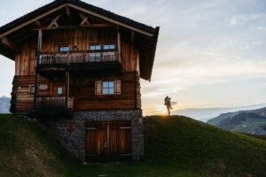 Silhouette of man and woman dancing around a wooden cabin in Alpe di Siusi at sunset