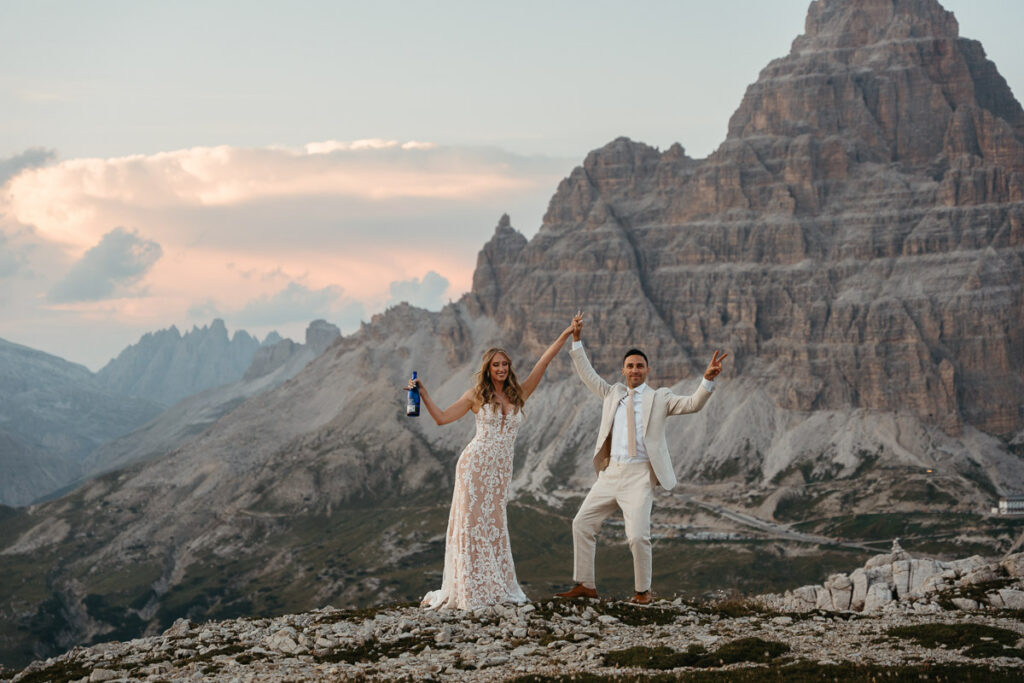 Husband and wife cheering to their vow renewal on Cadini di Misurina at sunset