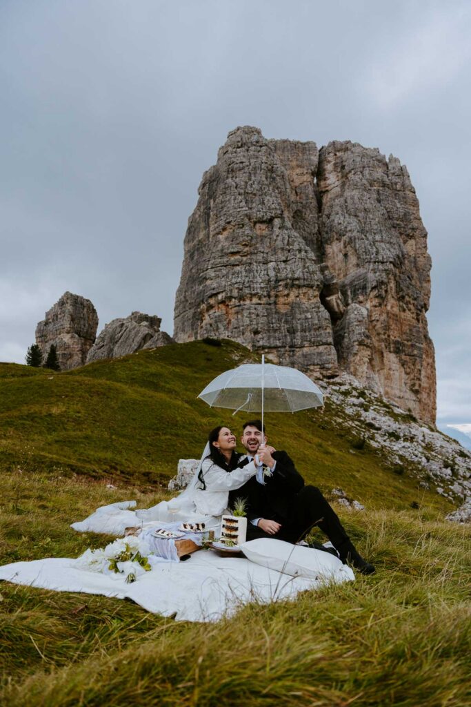 Bride and groom holding umbrella up at Cinque Torri in the Dolomites during their elopement. Why you should have a multi-day elopement.