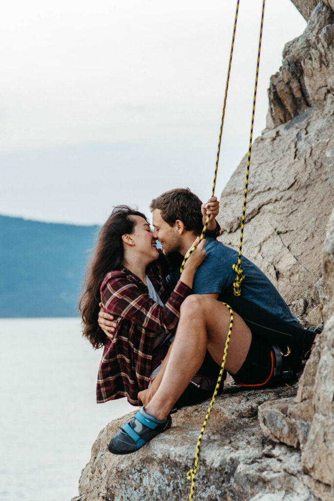 Adventurous rock climbing proposal at Lighthouse Park in Vancouver, couple on the ropes with the rocks and water in view