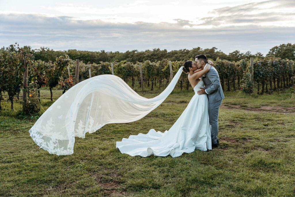 Bride and groom kissing against winery in Croatia with her veil sweeping in the wind
