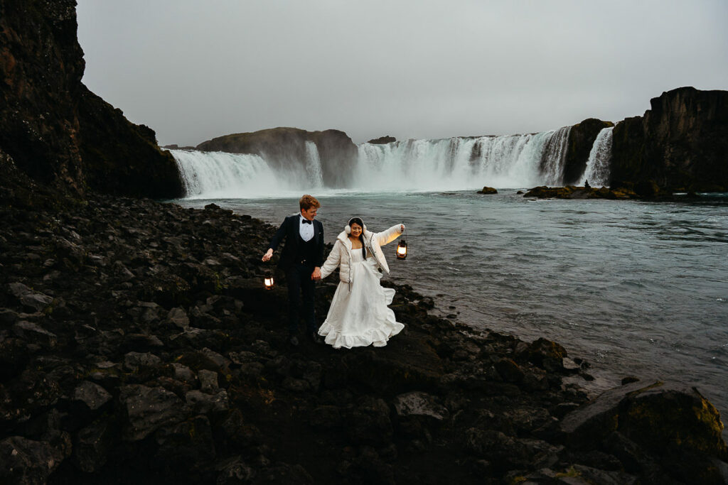 Bride and groom walking through black rocks on Iceland at Godafoss