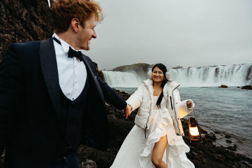 Groom looking back at bride and they are walking around Godafoss; How to Elope in Iceland