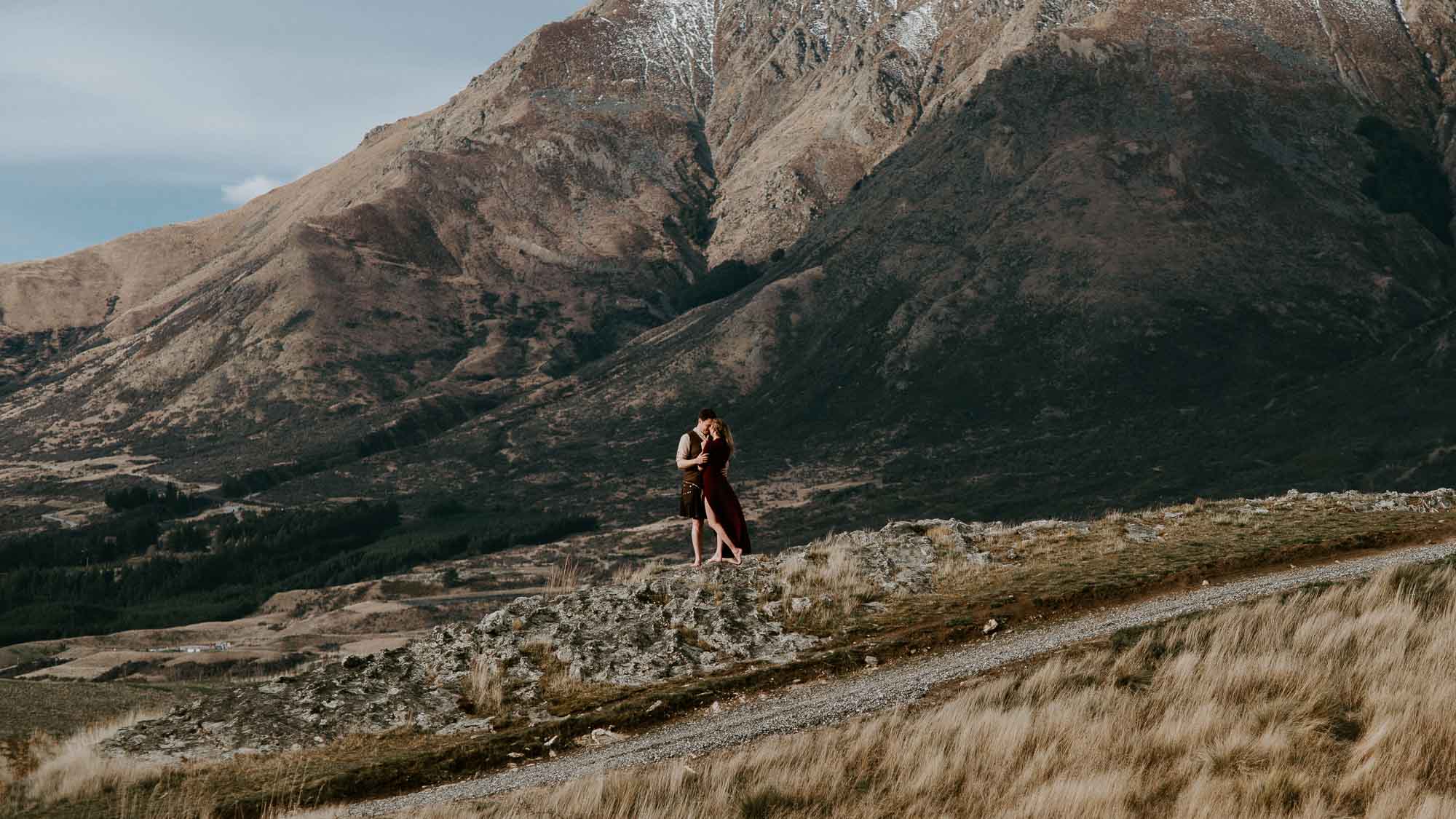 Bride and groom embracing in the wind at Jack's Point in Queenstown, New Zealand. Groom is wearing a kilt and bride a traditional Scottish dress.