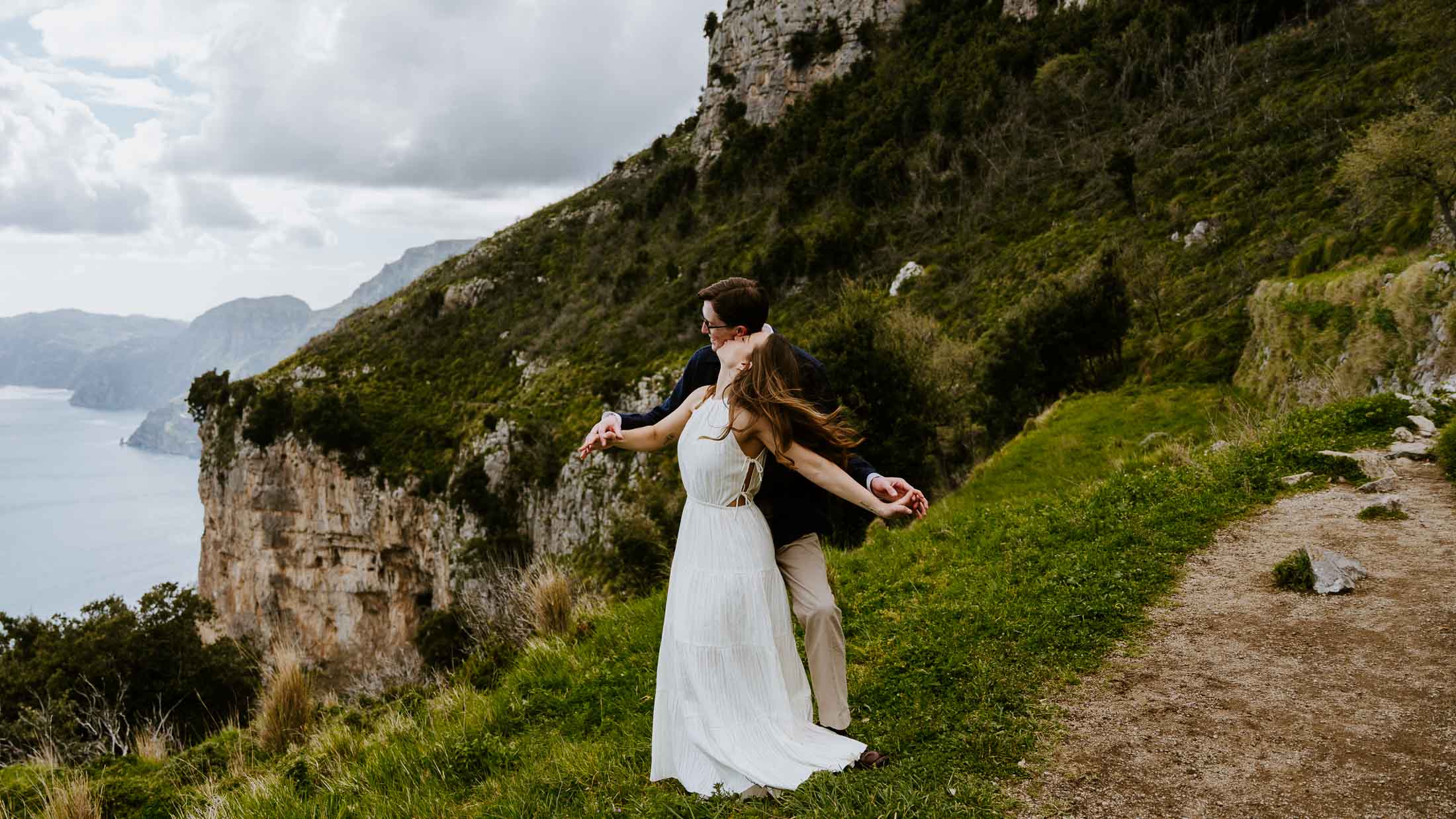 Groom holding bride from behind while they put their arms out like they're flying, along the Path of the Gods hike on the Amalfi Coast