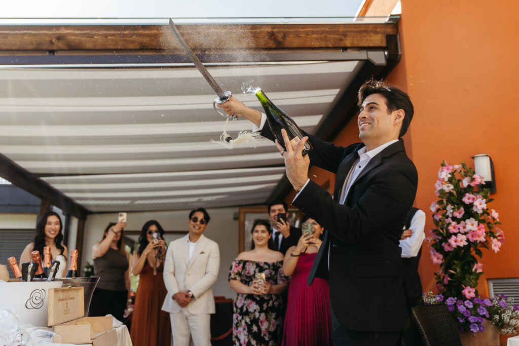 Groom cutting off champagne cork during intimate wedding in the Dolomites, including their best friends during their elopement day