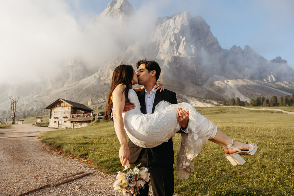 Bride and groom that I helped learn how to elope, he is holding her up and she's holding flowers at Passo delle Erbe
