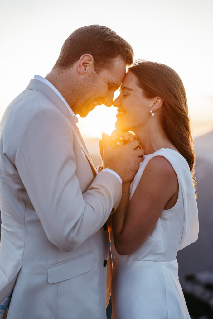 Bride and groom touching foreheads with backlit sunset shining through them on Cadini di Misurina. I helped them learn how ot Elope.