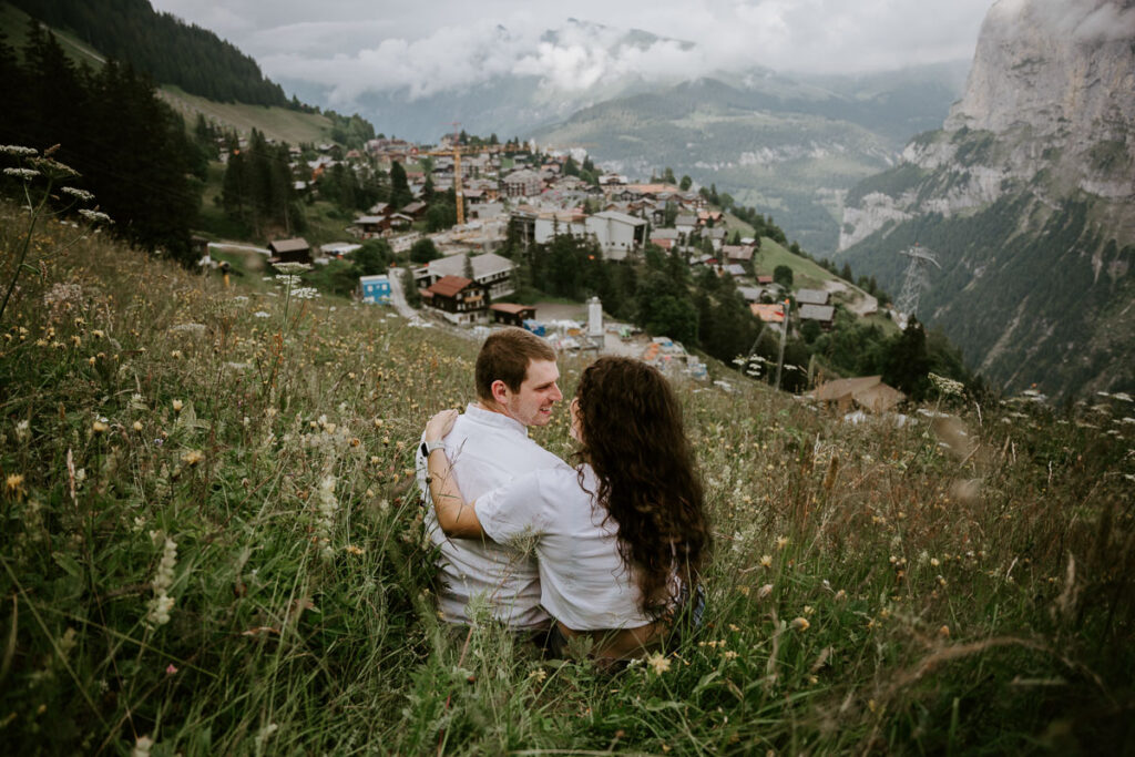 Man and wife enjoying the views in Mürren, sitting in a field; How to Elope in Switzerland